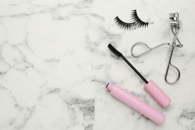 False eyelashes, curler and mascara on white marble table, flat lay. Space for text