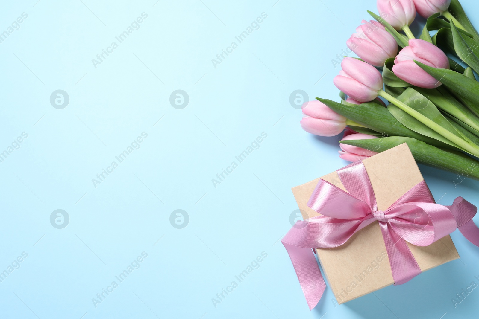 Photo of Beautiful gift box and bouquet of pink tulip flowers on light blue background, flat lay. Space for text