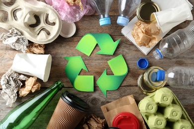 Photo of Recycling symbol and different garbage on wooden background, top view