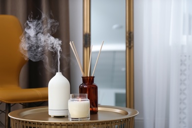 Photo of Aroma oil diffuser, air reed freshener and burning candle on table indoors, space for text. Interior elements