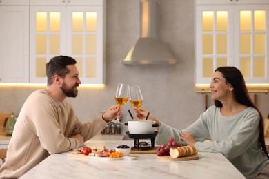 Photo of Romantic date with fondue. Couple clinking glasses of wine at home