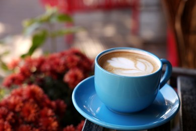 Photo of Ceramic cup of aromatic coffee with foam on wooden table in outdoor cafe. Space for text