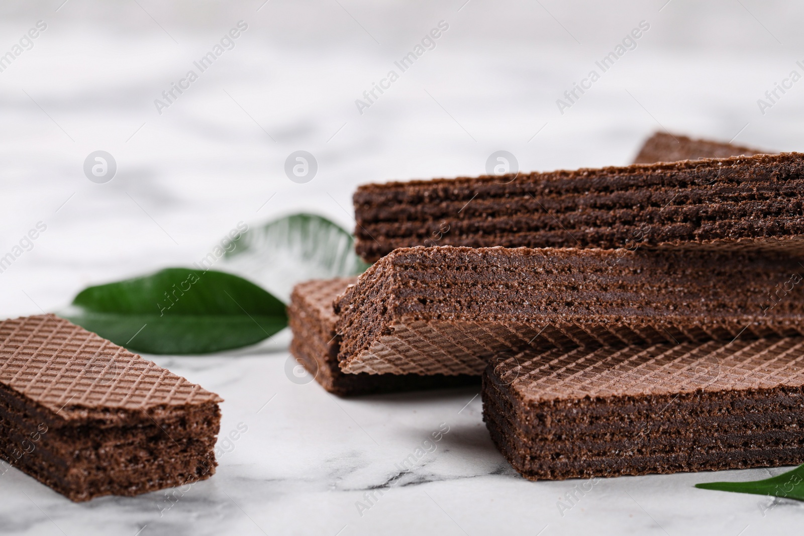 Photo of Delicious chocolate wafers with leaves on marble background, closeup