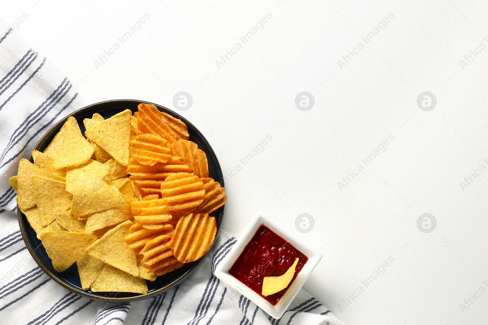 Photo of Tasty tortilla and ridged chips with ketchup on white table, flat lay. Space for text