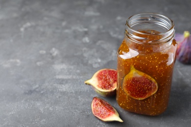 Photo of Delicious fig jam and fresh fruits on grey table, closeup. Space for text