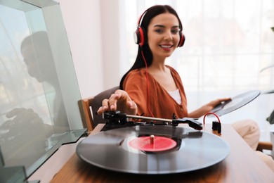 Photo of Woman listening to music with turntable at home, focus on hand
