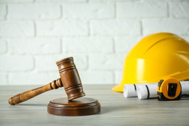 Photo of Construction and land law concepts. Judge gavel, protective helmet, drawings with tape measure on wooden table