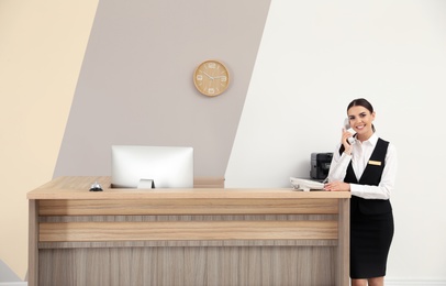 Photo of Receptionist talking on telephone near desk in modern hotel