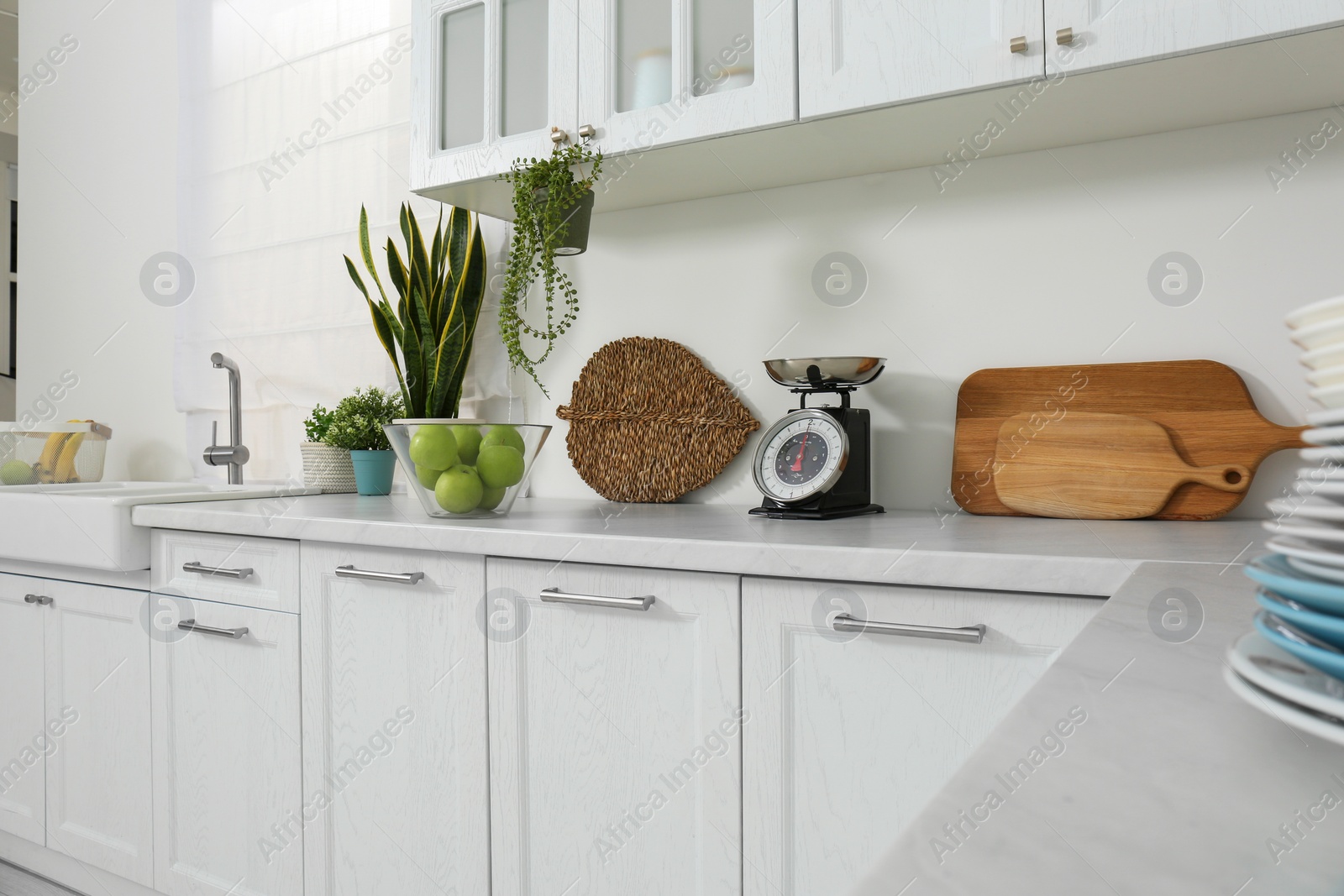 Photo of Stylish scale, apples and houseplants on white countertop in kitchen. Interior design