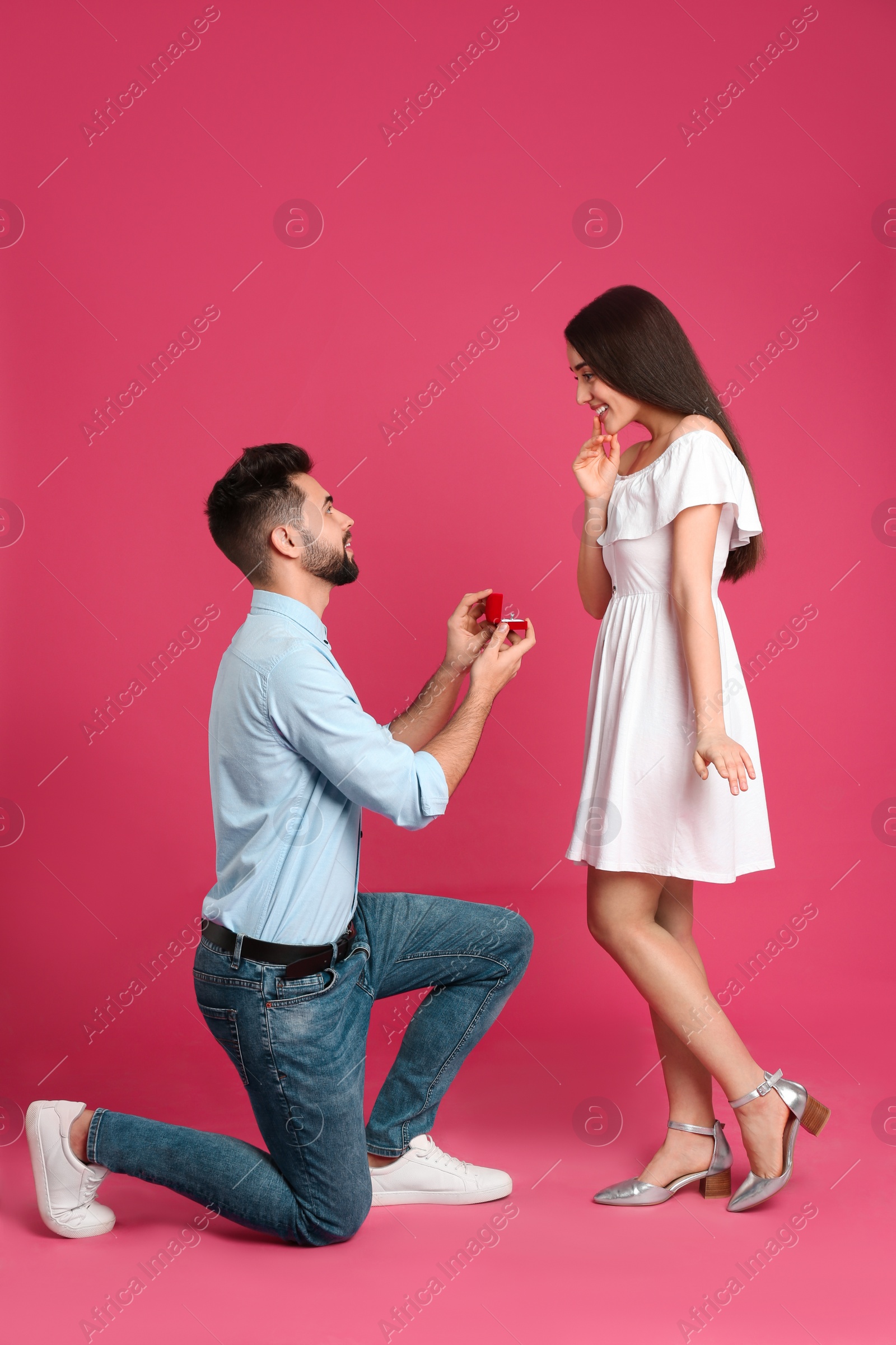 Photo of Man with engagement ring making marriage proposal to girlfriend on crimson background