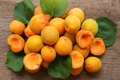 Photo of Delicious ripe apricots with green leaves on wooden table, top view