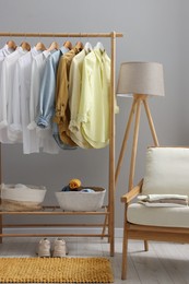 Photo of Wardrobe organization. Rack with different stylish clothes, armchair and lamp near grey wall indoors