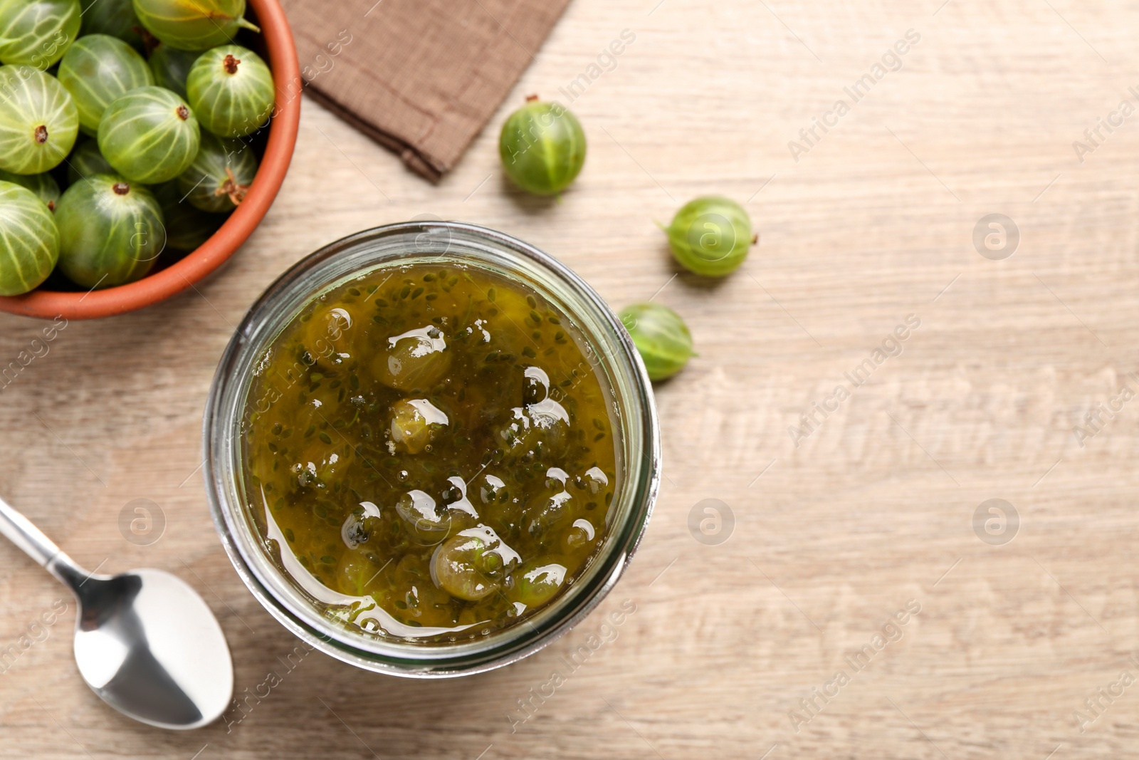 Photo of Jar of delicious gooseberry jam and fresh berries on wooden table, flat lay. Space for text