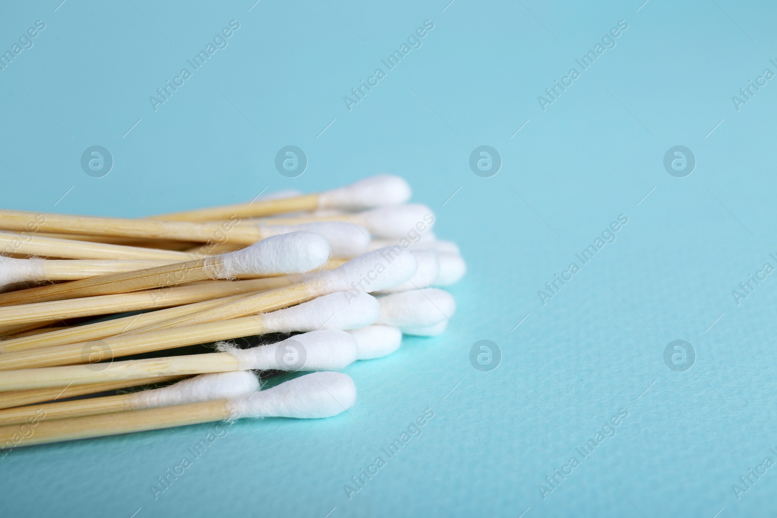 Photo of Wooden cotton buds on light blue background, closeup. Space for text