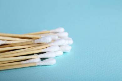 Photo of Wooden cotton buds on light blue background, closeup. Space for text