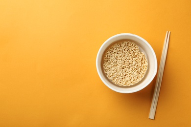 Cup of instant noodles with chopsticks on color background, top view. Space for text