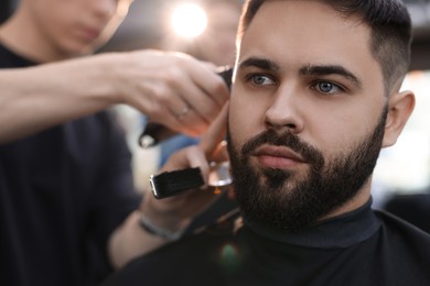 Photo of Professional hairdresser working with client in barbershop, closeup