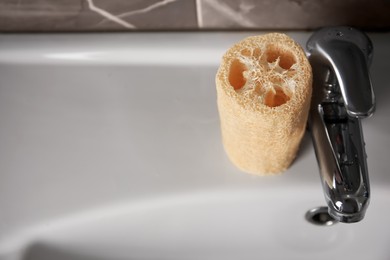 Photo of Natural loofah sponge on washbasin near faucet, above view