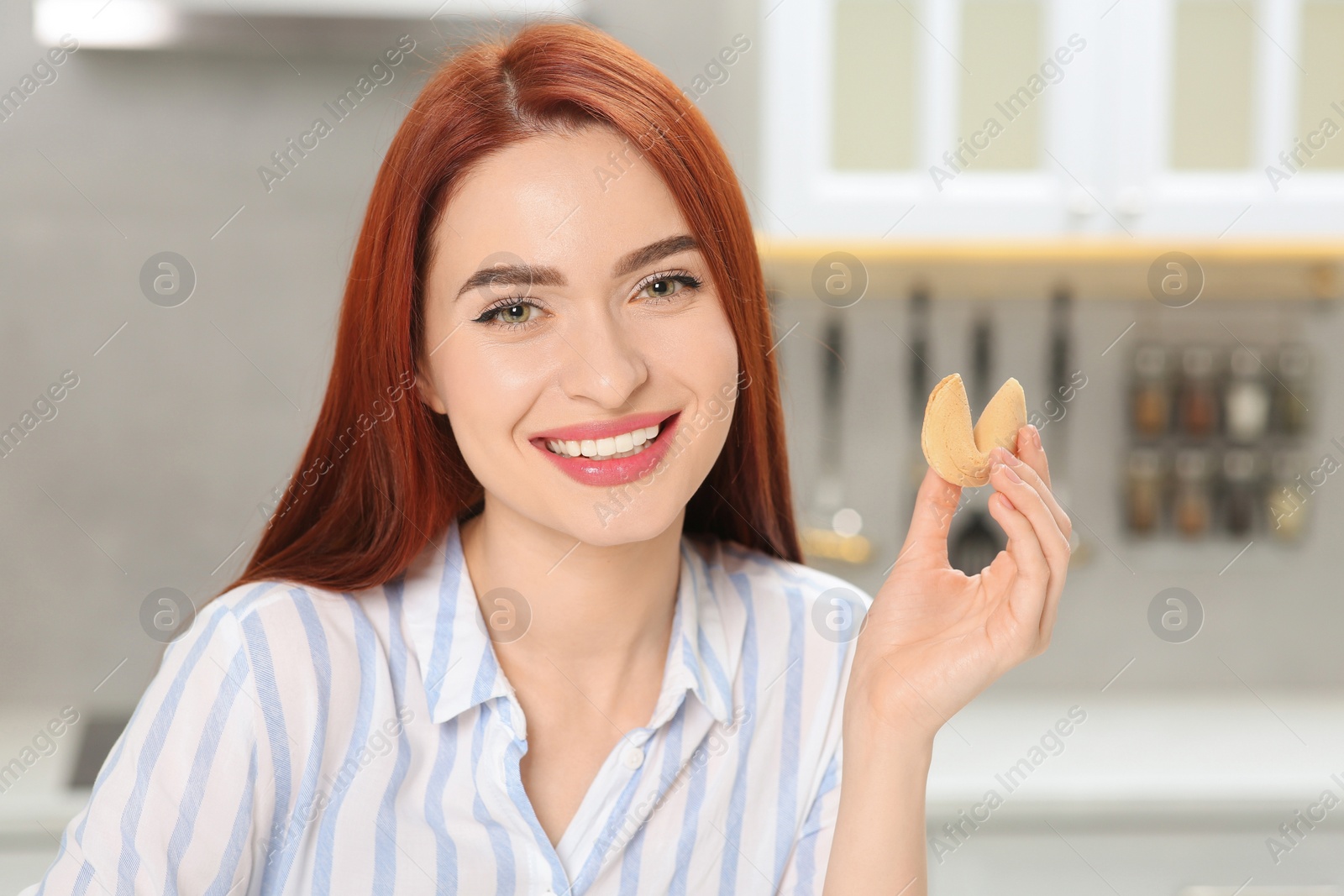 Photo of Happy woman with red dyed hair holding fortune cookie in kitchen