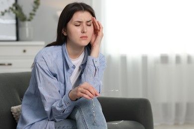 Overwhelmed woman with glasses sitting on sofa at home. Space for text