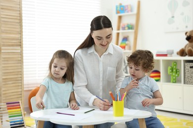 Photo of Mother and her little children drawing with colorful pencils at home