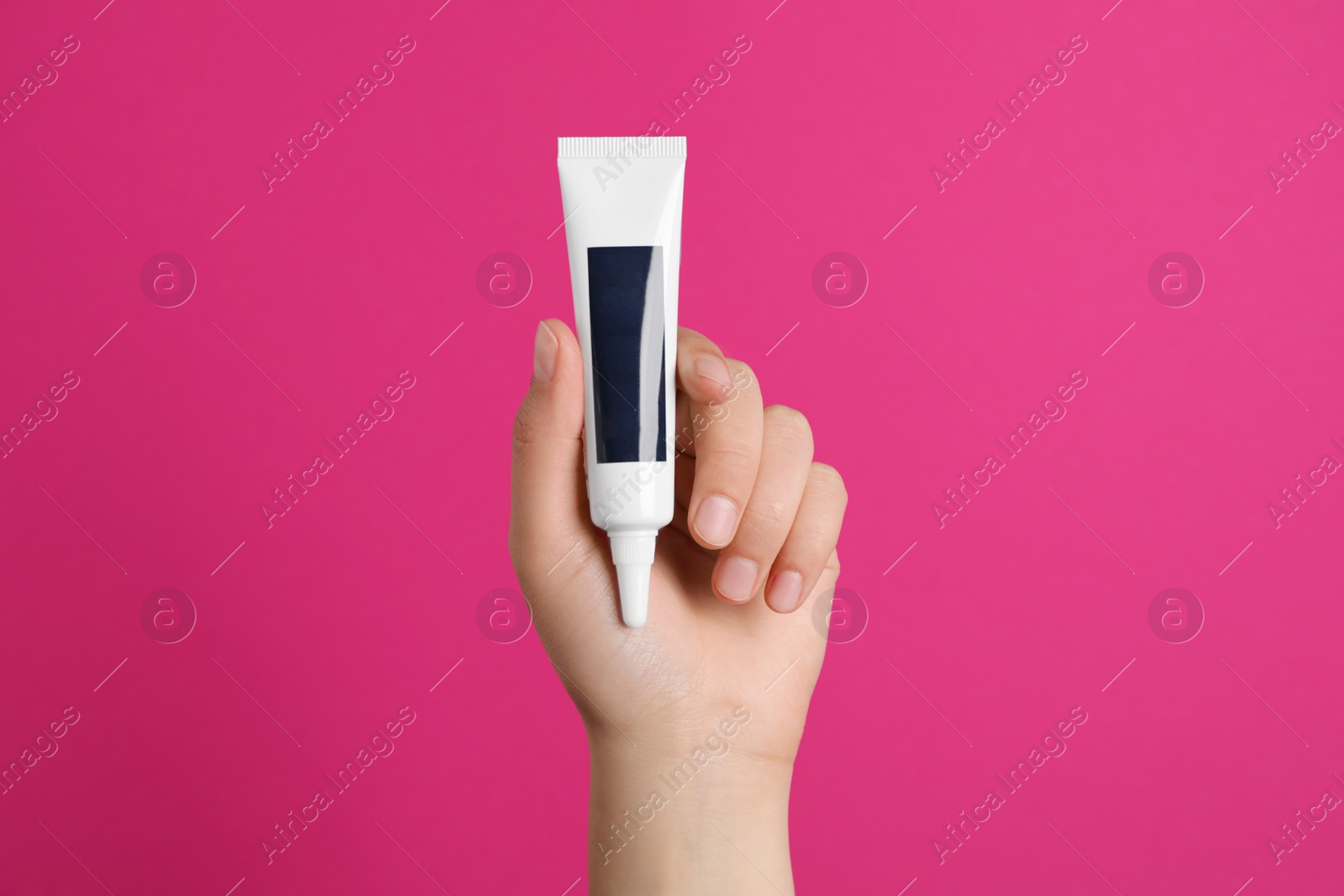 Photo of Woman holding tube of cream on pink background, closeup