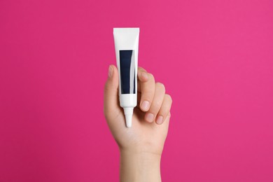 Photo of Woman holding tube of cream on pink background, closeup