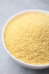 Photo of Raw couscous in bowl on gray table, closeup