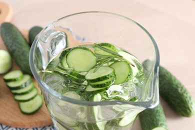 Photo of Refreshing cucumber water with rosemary in jug and vegetables on light table, closeup