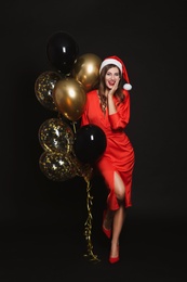 Photo of Happy woman in Santa hat with air balloons on black background. Christmas party
