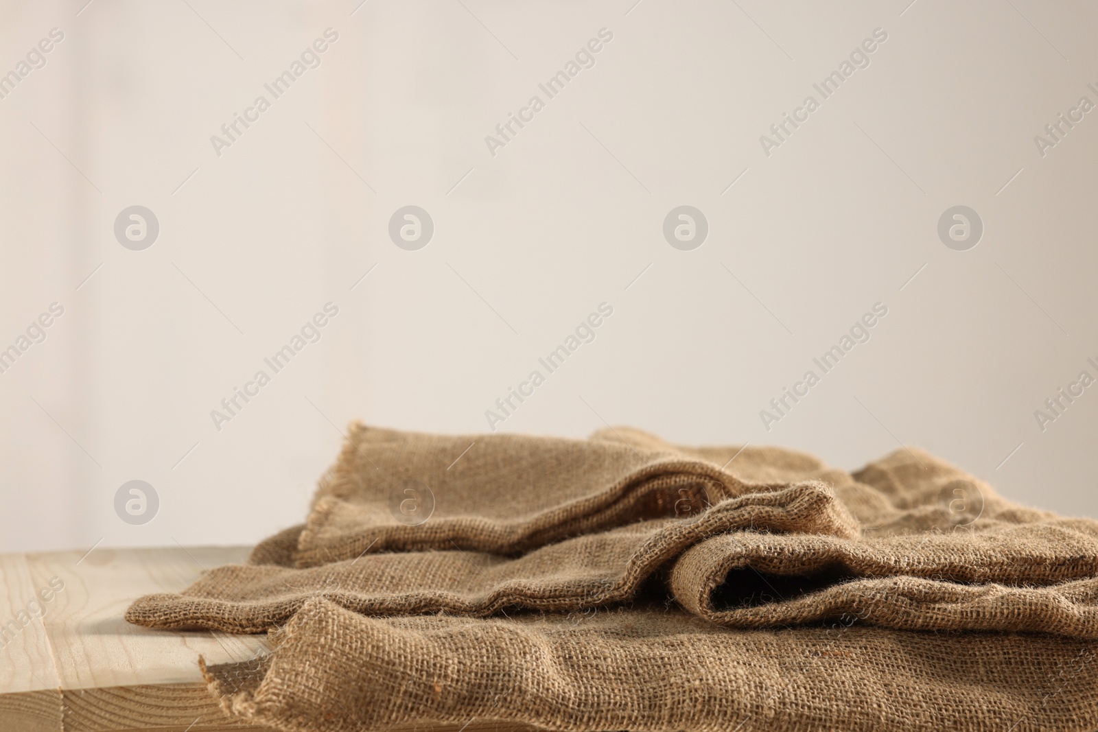 Photo of Natural burlap fabric on wooden table against light background. Space for text