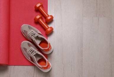 Photo of Dumbbells, sneakers and mat on wooden floor, above view. Space for text