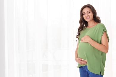 Beautiful pregnant woman near window at home