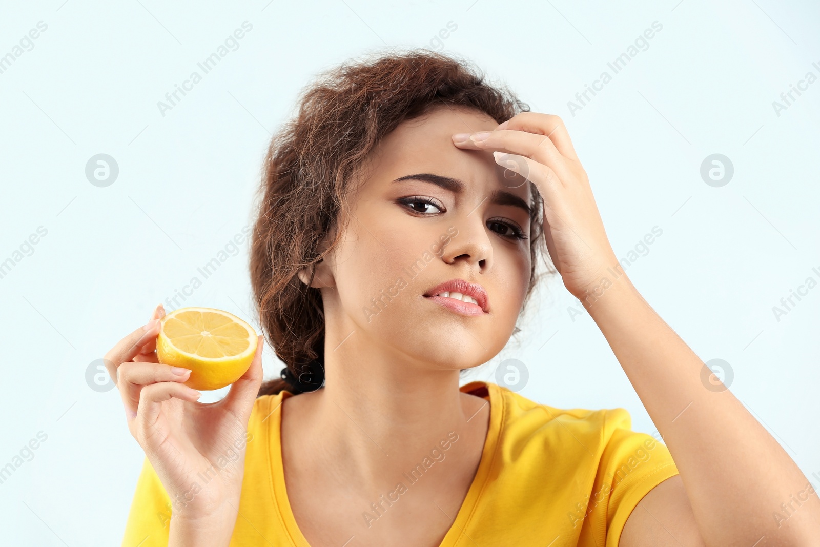 Photo of Beautiful young woman with acne problem holding lemon on light background. Skin allergy