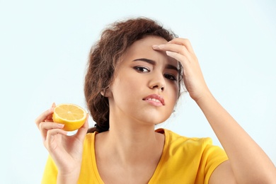 Beautiful young woman with acne problem holding lemon on light background. Skin allergy