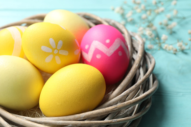 Colorful Easter eggs in decorative nest on light blue wooden table, closeup