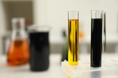 Photo of Test tubes with different types of crude oil against blurred background, closeup. Space for text