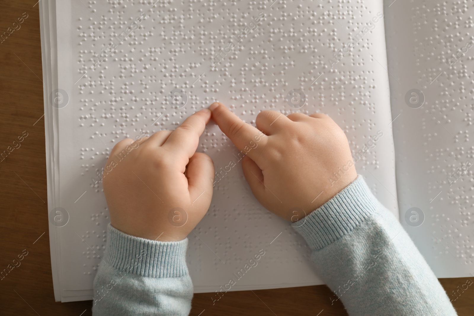 Photo of Blind child reading book written in Braille at table, top view