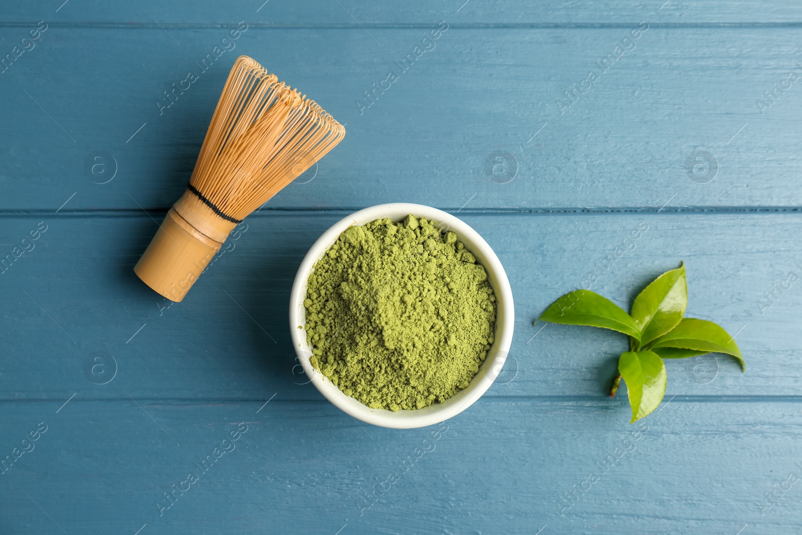 Photo of Matcha tea in bowl, whisk and green leaves on wooden table, top view