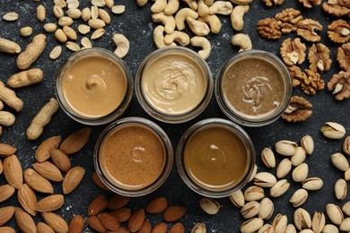 Photo of Tasty nut butters in jars and raw nuts on dark gray table, flat lay