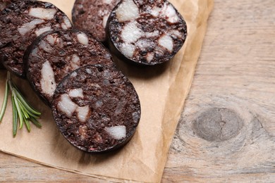 Photo of Slices of tasty blood sausage with rosemary on wooden table, closeup