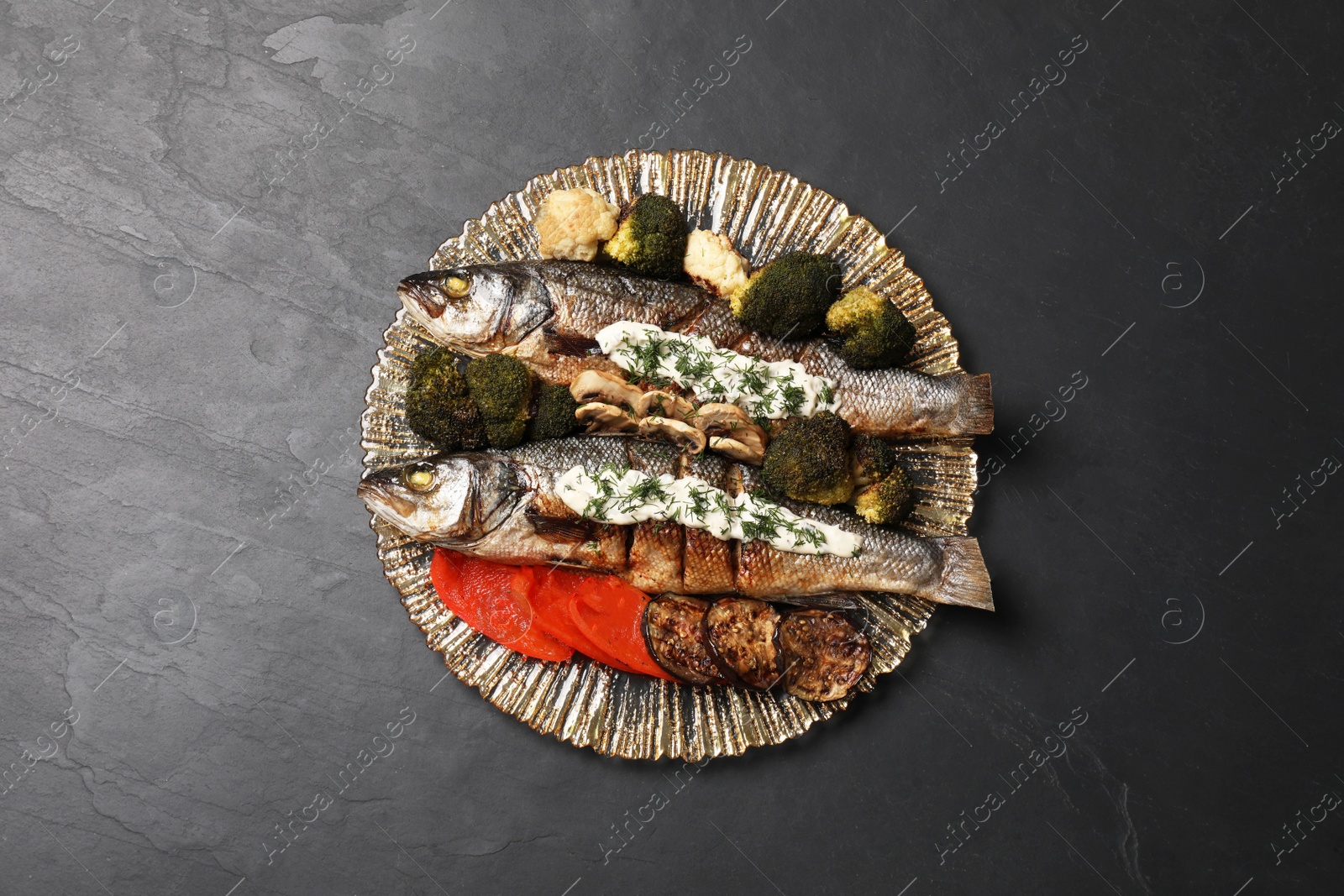 Photo of Plate with delicious sea bass fish and ingredients on dark grey table, top view