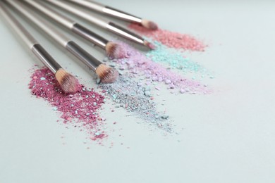 Photo of Different makeup brushes with crushed cosmetic products on light background. Space for text