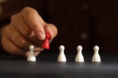 Choice concept. Woman choosing red pawn among white ones at black table, closeup