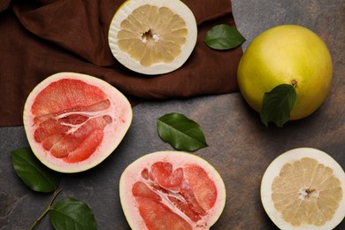 Photo of Fresh cut and whole pomelo fruits with green leaves on dark table, flat lay