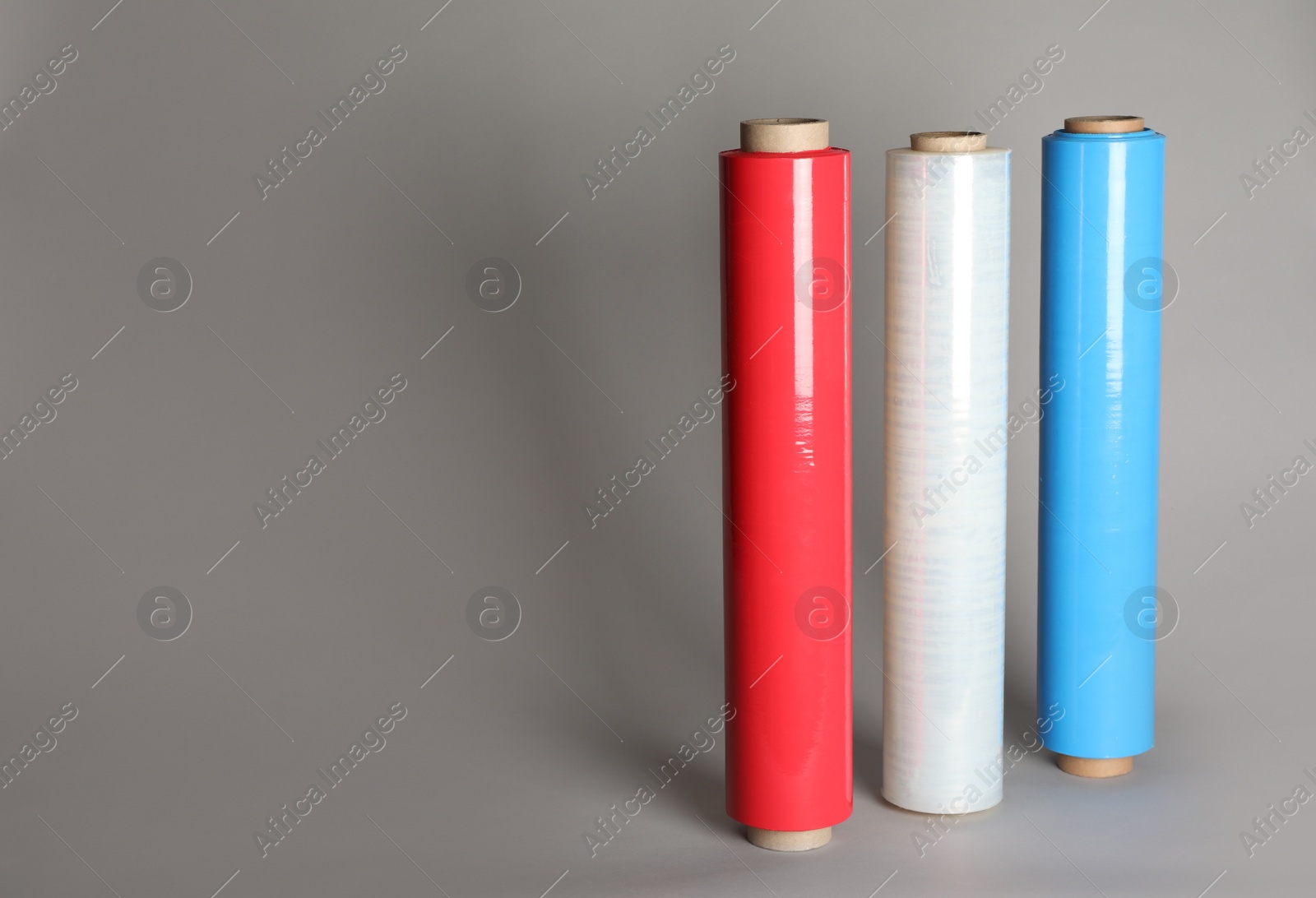 Photo of Different plastic stretch wrap films on grey background, space for text