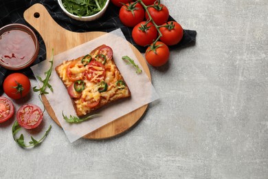 Tasty pizza toast, sauce, tomatoes and arugula on grey table, top view. Space for text
