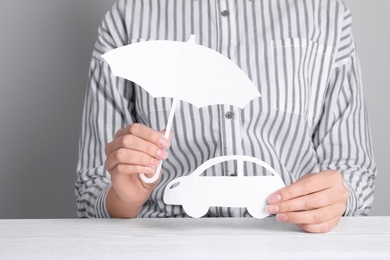 Photo of Insurance agent covering paper car with umbrella cutout at table, closeup