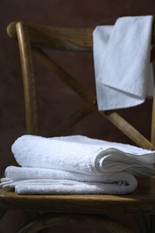 Photo of White terry towels on wooden chair against brown background, closeup