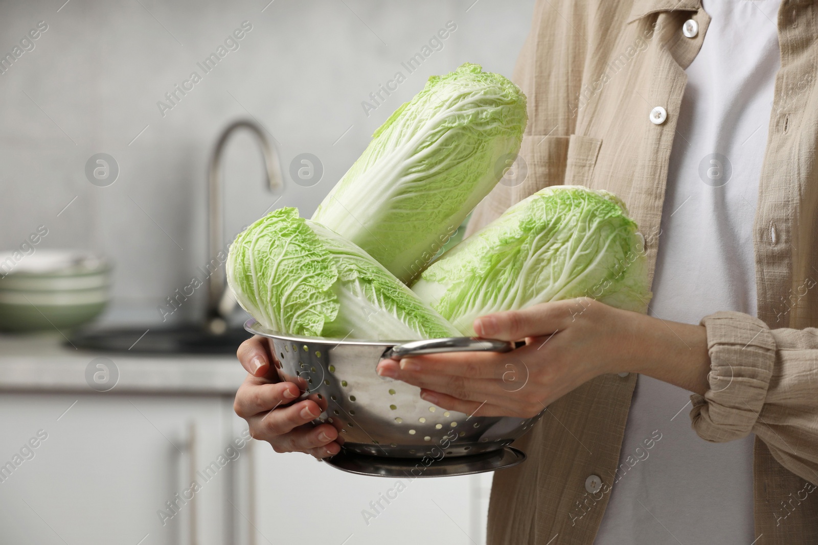 Photo of Woman holding fresh chinese cabbages in kitchen, closeup. Space for text